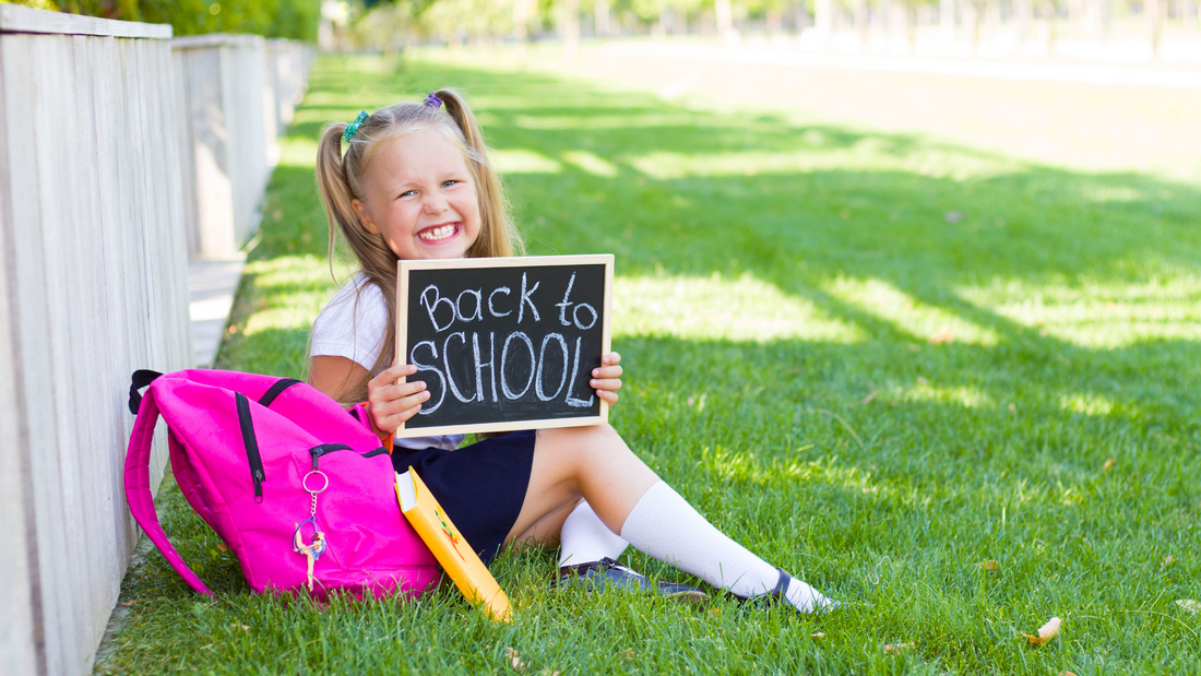 little girl smiling sitting in grass holding back to school sign